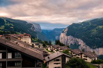 Fototapeta na wymiar View on swiss alpine village Wengen and the cliffs of the Lauterbrunnen valley under cloudy skies in morning in summer