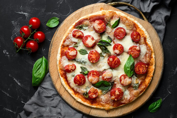 Traditional italian pizza Margherita on a wooden cutting board, black stone background. Pizza with tomato, mozzarella and basil. Top view, flat lay.