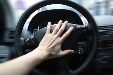 A panicking hand pushing the steering wheel of a car whilst driving. Honking the horn can be used to avoid an accident in a dangerous situation. The car is clearly driving fast, or is even speeding. - obrazy, fototapety, plakaty
