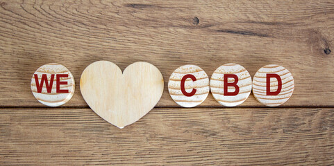 Concept words 'we' and 'cbd' on wooden circles. Wooden heart. Beautiful wooden background.