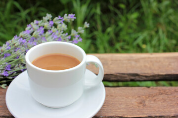 Cup of coffee with milk or cappuccino and lavender flowers on wooden board in summer garden. Enjoying morning coffee. Top view, copy space. Selective focus