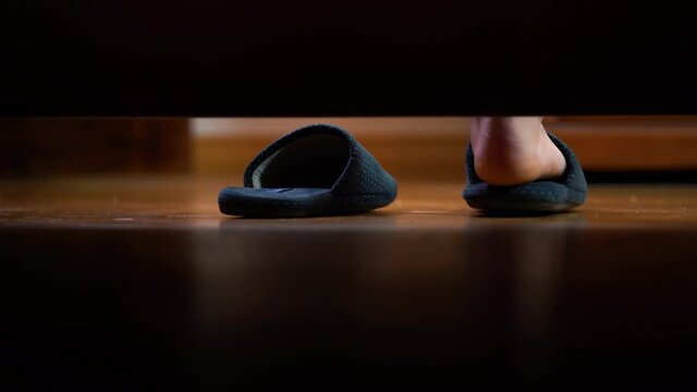 Slippers on the floor.Man's foot put on slippers on the floor. Camera's view from under the bed.