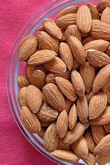 Fototapeta premium Fragment of a glass plate with almond kernels on a red tablecloth