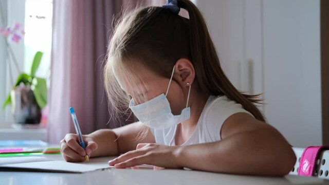 Close up of girls hands write on a sheet of paper. Writing an essay or letters. A schoolboy writes in a notebook. He does lessons in a medical mask. Doing homework.