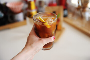 Espresso tonic with lemon slice in bid glass with ice in female hand close up
