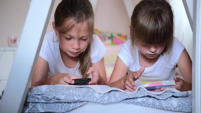 Happy little girl or child playing at home, relax, use a smartphone, sit on the couch daughter, look at the tablet screen, watch cartoons.