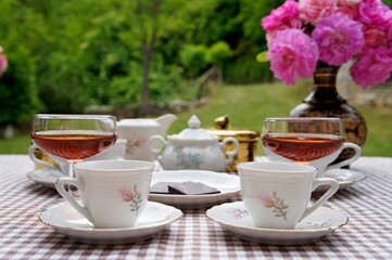 two cups of coffee, martini glasses and pink roses flowers on the table in the garden