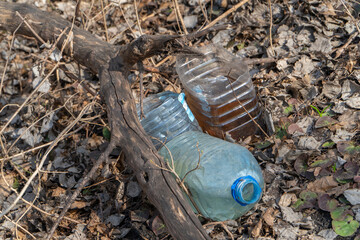 Fototapeta premium Three big plastic bottles lie on last year leaves near dead branch. Spring forest polluted by human rubbish recyclable litter. Ecology concept of the dangerous garbage. Horizontal image, copy space.
