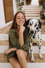 Long hair, freckled young girl sitting on a step in a green blouse playing with her Dalmatian dog
