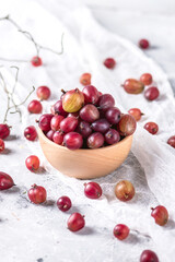 Wooden bowl with fresh sweet gooseberries on light background