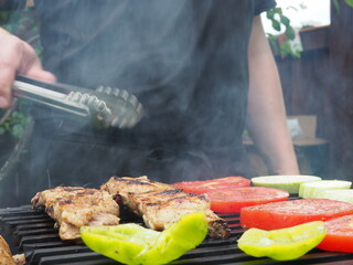 the cook turns vegetables with meat tongs on the grill on the coals. delicious food.
