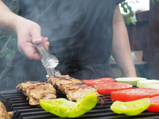 the cook turns vegetables with meat tongs on the grill on the coals. delicious food.