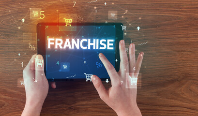 Close-up of a hand holding tablet with FRANCHISE inscription, online shopping concept