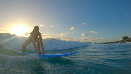 SUN FLARE: Woman learning to surf stands up on her longboard and rides a wave