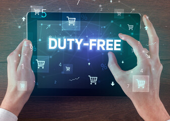 Close-up of a hand holding tablet with DUTY-FREE inscription, online shopping concept