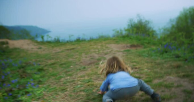 A little preschooler is walking in a meadow by the sea and falls