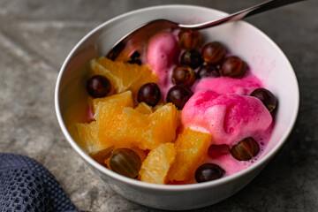 Summer refreshing dessert with fruit and berries. Pink ice cream in a bowl with orange pulp and gooseberry berries.