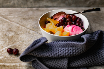 Summer refreshing dessert with fruit and berries. Pink ice cream in a bowl with orange pulp and gooseberry berries.