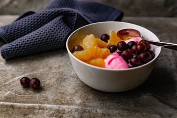 Summer refreshing dessert with fruit and berries. Pink ice cream in a bowl with orange pulp and gooseberry berries.