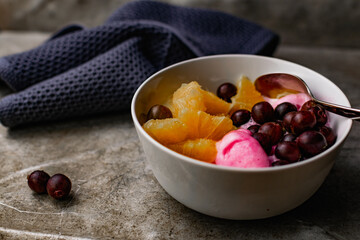 Summer refreshing dessert with fruit and berries. Pink ice cream in a bowl with orange pulp and gooseberry berries.
