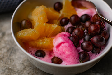 Summer refreshing dessert with fruit and berries. Pink ice cream in a bowl with orange pulp and gooseberry berries.
