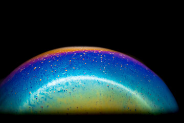 Close up macro of one colorful soap bubble on a black dark background with abstract patterns. Looks like a planet in space