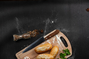 fresh white bread on a cutting board with seasonings  sprinkled with flour on a black wooden table