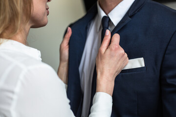 Caucasian woman straightens businessman's collar. Passionate flirting business people. Love affair in office. Close up shot.