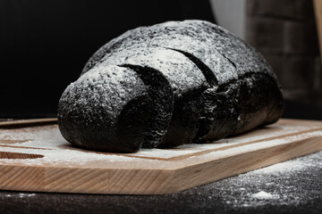 fresh black rye bread on a cutting board with flour on a black wooden table