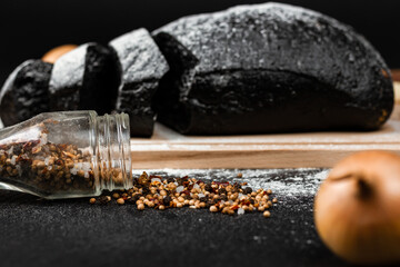 fresh black rye bread on a cutting board with seasonings  sprinkled with flour on a black wooden table