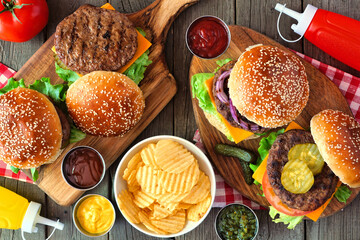 Summer BBQ hamburger table scene. Above view over a dark wood background.