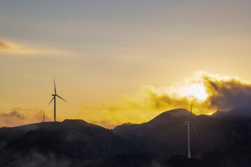 High in the mountains are wind turbines at sunrise and sunset and a sea of clouds