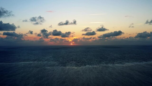 Beautiful aerial dolly in drone shot of a serene ocean sunrise at Well Beach near Joao Pessoa on a warm summer morning with the water below and golden clouds on the skyline.