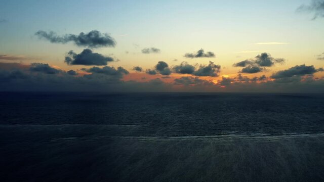 Beautiful aerial drone shot of a serene ocean sunrise at Well Beach near Joao Pessoa on a warm summer morning with the water below and golden clouds on the skyline.