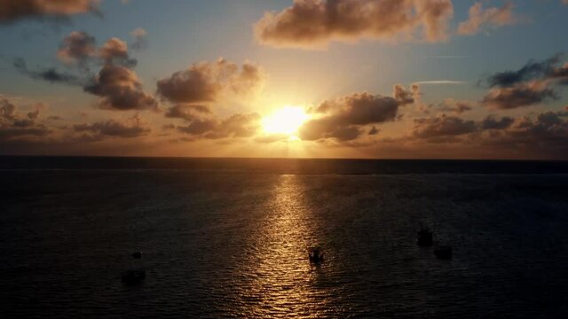 Beautiful aerial drone shot of an ocean sunrise at Well Beach near Joao Pessoa on a warm summer morning with the water below, golden clouds on the skyline, and small boats in the water.