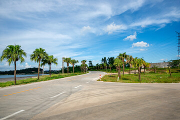 The road in the tropical park is under the blue sky and white clouds