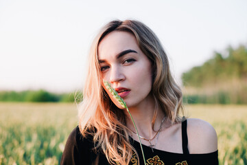 Naklejka premium Young, slender girl embroidered dress in a large wheat field at sunset