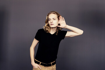 Attractive guy with long blonde hair, substituting a hand to his ear, eavesdrops with an interested...