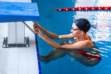 Young woman swimmer in a swimsuit getting ready to start a swimming in a swimming pool....
