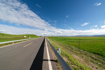 A straight asphalt road under the blue sky and white clouds