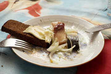     Bread and butter, two pieces of herring and finely chopped onions are on a plate with a knife and fork, ready to eat.