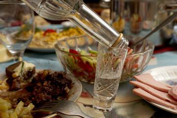       An empty bottle and a half empty glass on a table background full of snacks and dishes.