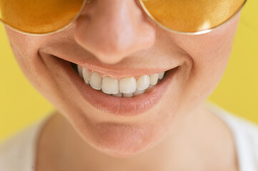 Close-up of a female smile on a yellow background. Cropped photo. Woman with a perfect smile in sunglasses.