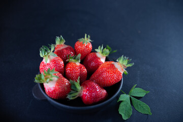 Fresh juicy strawberries in a black plate on a black matte background