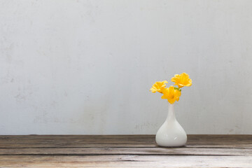 yellow day-lily flowers in white vase on wooden table