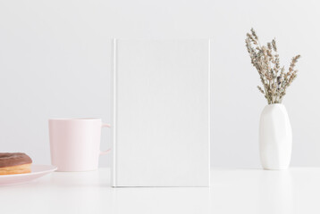 White book mockup with a mug, donut and lavanda in a vase on a white table.