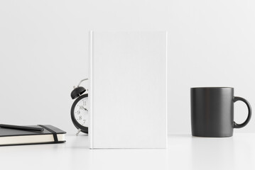 White book mockup with a mug, clock and notebook on a white table.