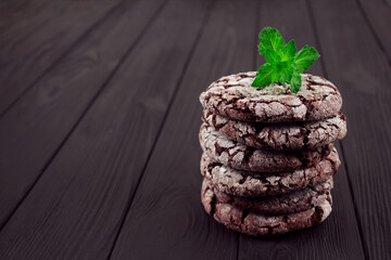 Stack of delicious chocolate cookies with fresh green mint topped with sugar on black wooden background with copyspace for text or recipe. Handmade gingersnap traditional cookies on rustic table