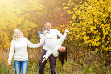 Naklejka na ściany i meble Picture of lovely family in autumn park, young parents with nice adorable daughter playing outdoors, have fun on backyard in fall, happy family enjoy autumnal nature