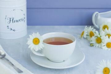 Herbal chamomile tea with fresh chamomile flowers in a white cup and saucer on a light background. A linen towel and a teaspoon.